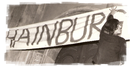 Altes Schwarzweiß-Foto. Junger Student hängt ein Transparent mit dem Schriftzug "HAINBURG" auf.