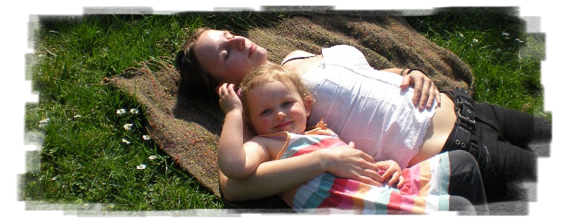 Eine junge Frau und ein kleines Kind liegen in der Wiese in der Sonne und genießen den Garten.
